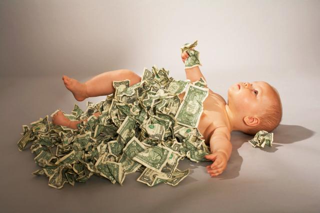 baby laying on its back blanketed with crumpled dollar bills