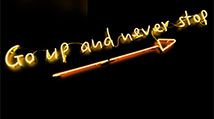 Illuminated yellow neon sign on black background with an upward arrow saying GO Up and Never Stop