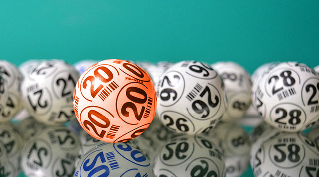  A jumble of numbered lotto balls in a pile. One stands out because it is orange.