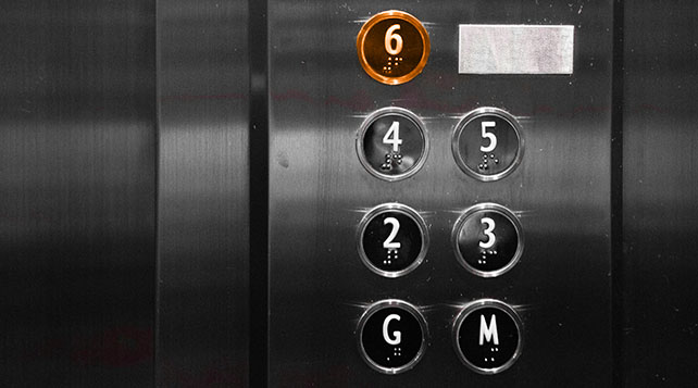 Elevator button panel with the 6th floor button illuminated in orange