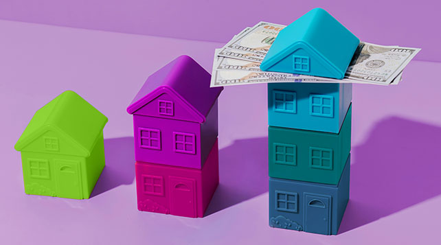Plastic blocks in the shape of homes: green, pink, blue. One has dollar bills sandwiched under the roof.