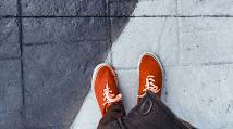 orange tennis shows between two contrasting colors of light and grey pavement